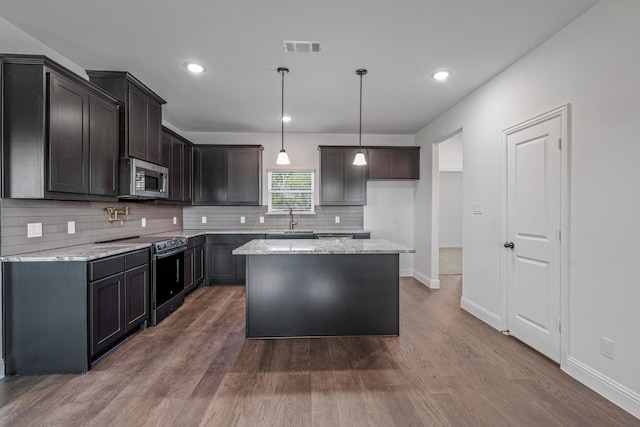 kitchen featuring a sink, decorative backsplash, range with electric stovetop, stainless steel microwave, and baseboards