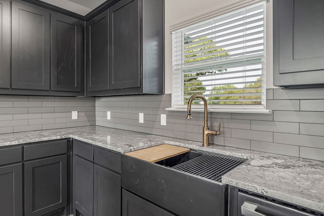 kitchen featuring a sink, backsplash, light stone counters, gray cabinets, and dishwasher
