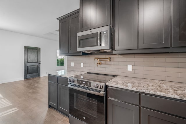 kitchen featuring tasteful backsplash, light stone counters, light wood-type flooring, baseboards, and appliances with stainless steel finishes