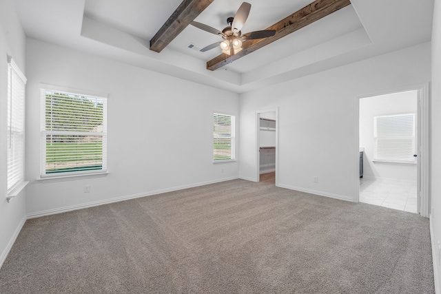 unfurnished bedroom with beam ceiling, baseboards, carpet, a walk in closet, and a raised ceiling