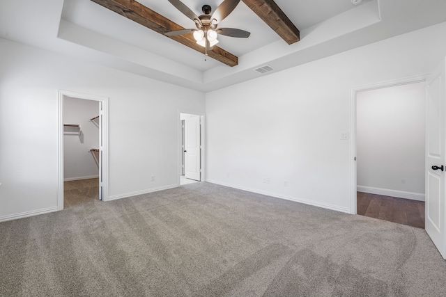 unfurnished bedroom featuring carpet, a spacious closet, visible vents, beamed ceiling, and baseboards