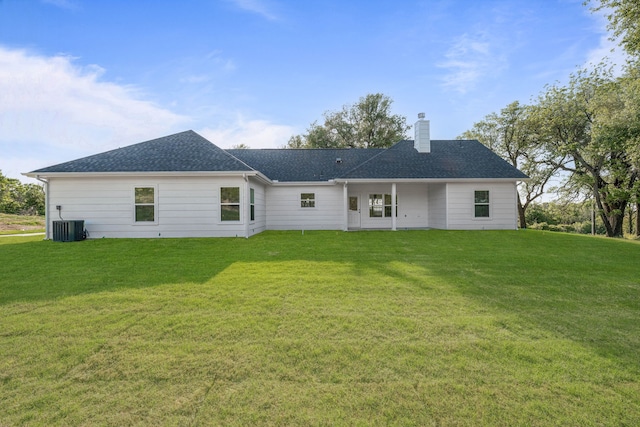 rear view of house with a lawn, central AC unit, a chimney, and a shingled roof