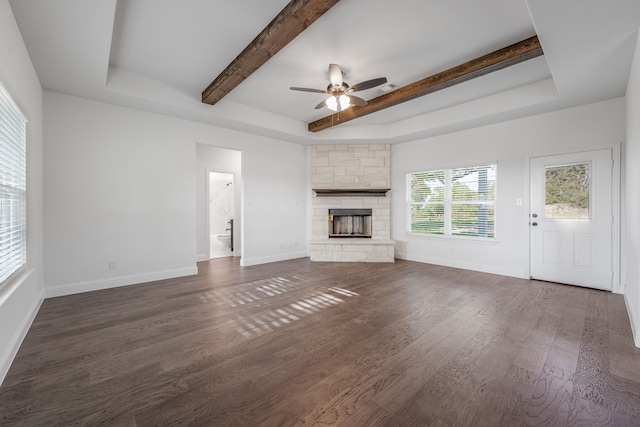 unfurnished living room featuring a tray ceiling, beam ceiling, dark wood finished floors, a ceiling fan, and a fireplace