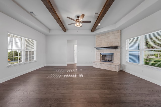 unfurnished living room with a stone fireplace, ceiling fan, beamed ceiling, dark wood-style flooring, and visible vents