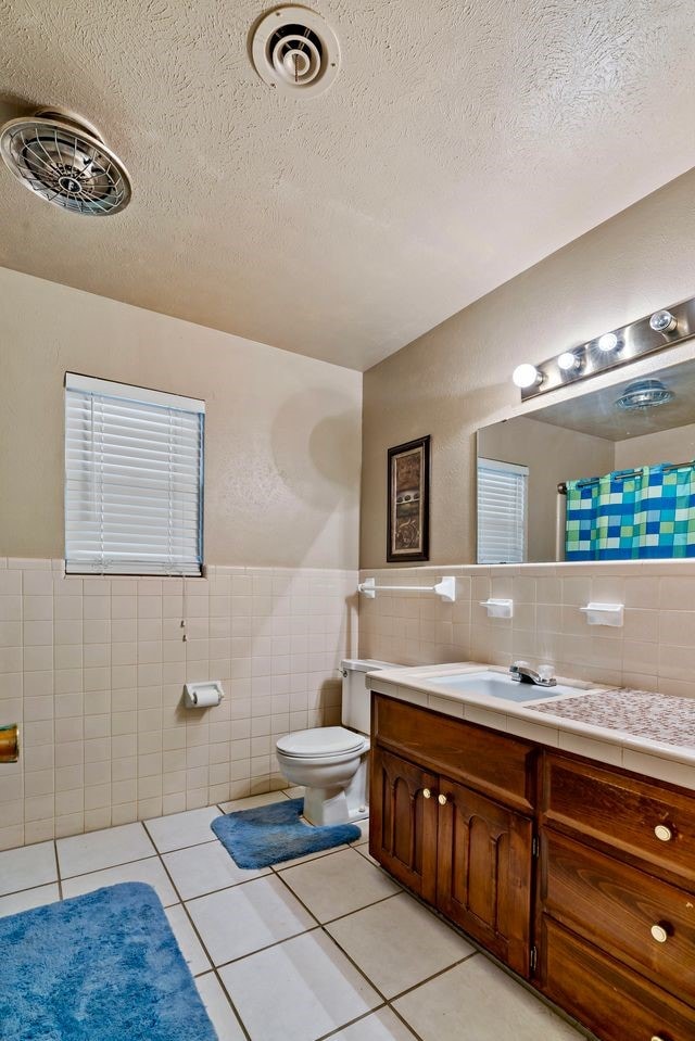 bathroom with tile patterned floors, toilet, vanity, tile walls, and a textured ceiling