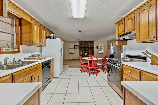 kitchen featuring a fireplace, black dishwasher, stainless steel stove, sink, and a textured ceiling