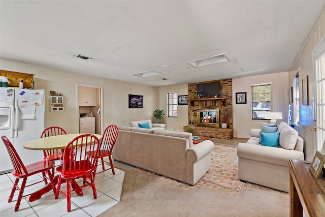 living room featuring light carpet, a textured ceiling, washer / clothes dryer, and a brick fireplace