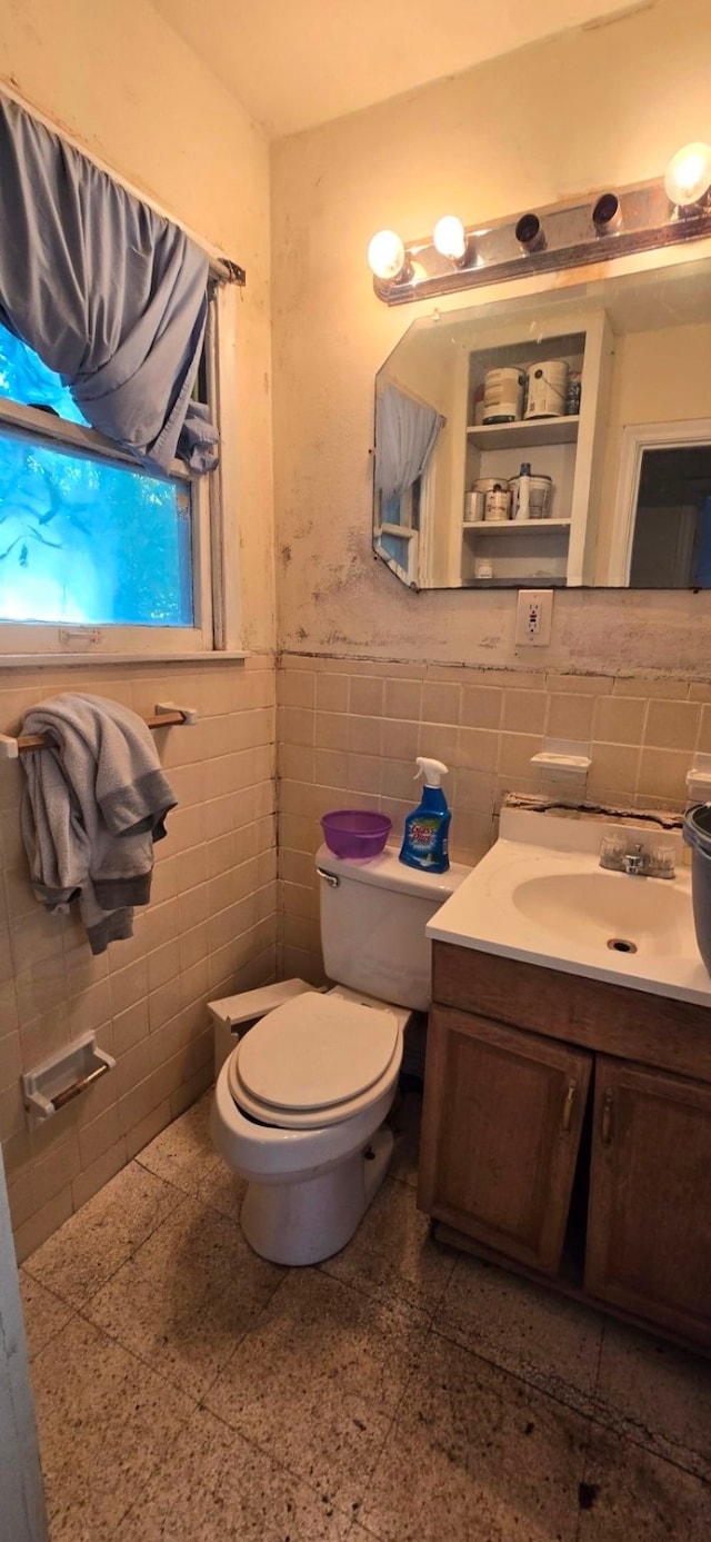 bathroom with toilet, vanity, and tile walls