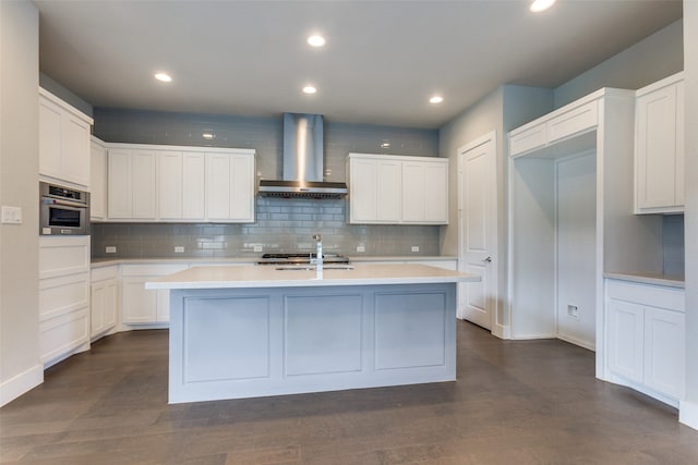 kitchen with wall chimney range hood, dark hardwood / wood-style flooring, and an island with sink