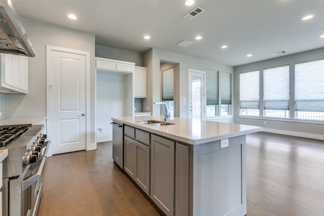 kitchen featuring gray cabinetry, a center island with sink, wall chimney range hood, stainless steel appliances, and dark hardwood / wood-style floors