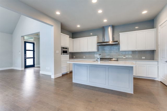 kitchen featuring oven, wall chimney exhaust hood, white cabinetry, and a center island with sink