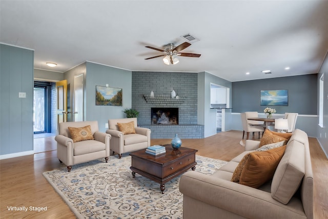 living room featuring light hardwood / wood-style floors, ceiling fan, and a brick fireplace