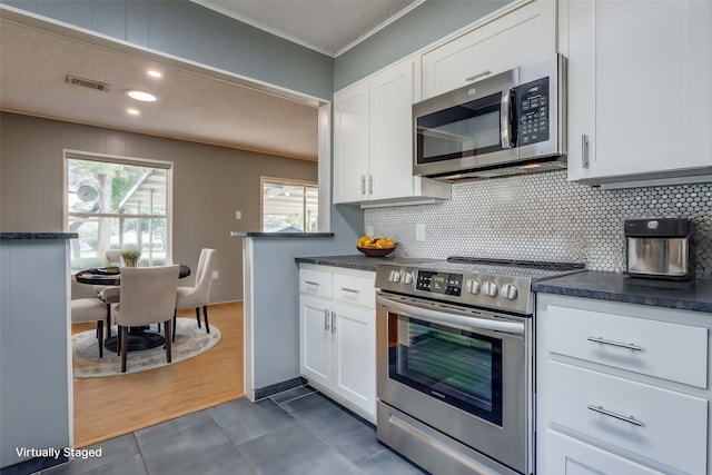 kitchen with dark hardwood / wood-style floors, backsplash, ornamental molding, white cabinetry, and appliances with stainless steel finishes