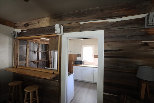 interior space with white cabinetry, wood walls, a kitchen bar, and light hardwood / wood-style flooring