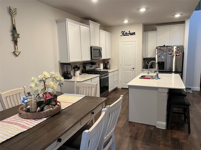 kitchen with appliances with stainless steel finishes, sink, white cabinetry, dark hardwood / wood-style floors, and a kitchen island with sink