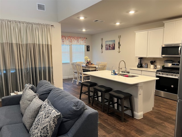 kitchen with white cabinets, a center island with sink, dark wood-type flooring, sink, and stainless steel appliances