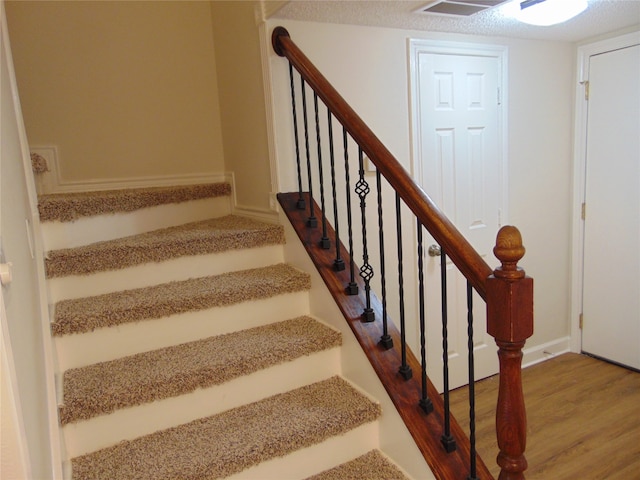 stairway with wood-type flooring and a textured ceiling