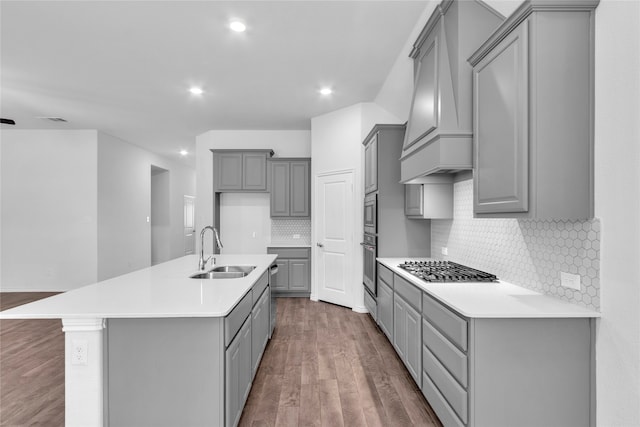 kitchen with gray cabinetry, a center island with sink, sink, hardwood / wood-style floors, and custom exhaust hood