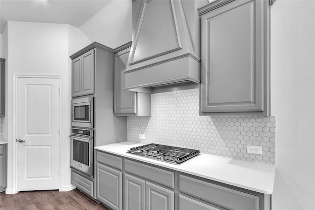 kitchen featuring decorative backsplash, custom range hood, stainless steel appliances, gray cabinets, and dark hardwood / wood-style flooring