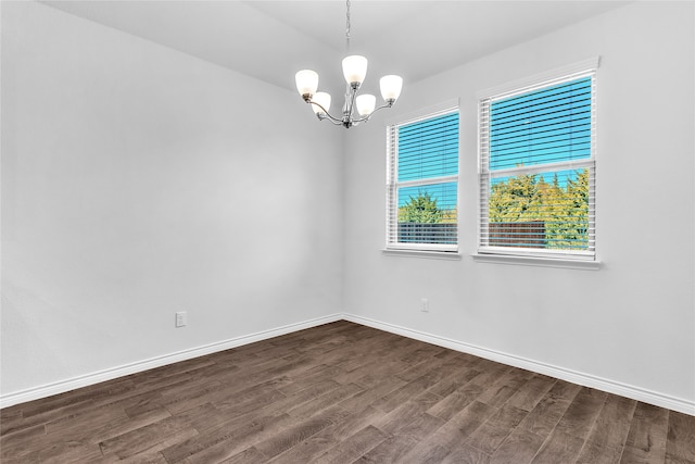 empty room with dark wood-type flooring, a healthy amount of sunlight, and an inviting chandelier