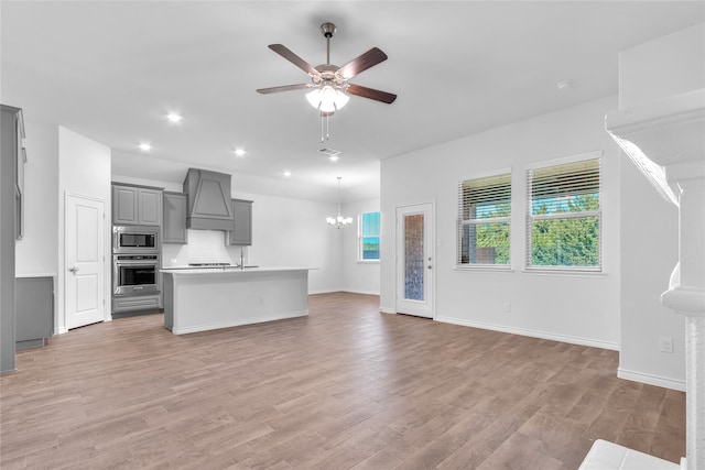 kitchen featuring an island with sink, custom range hood, gray cabinetry, stainless steel appliances, and light hardwood / wood-style floors