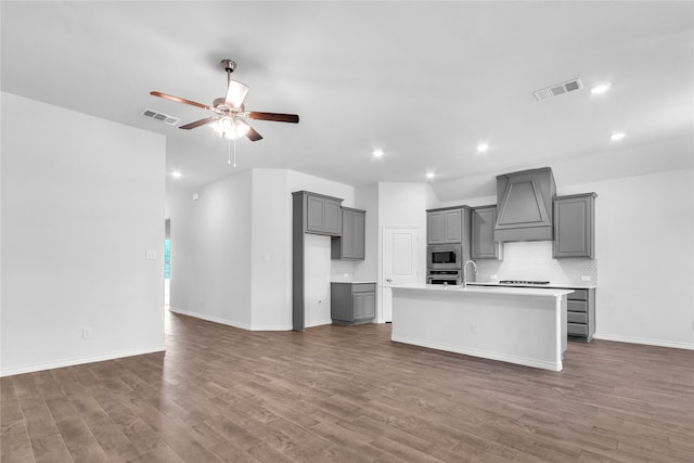 kitchen with dark hardwood / wood-style flooring, premium range hood, a center island with sink, and gray cabinets