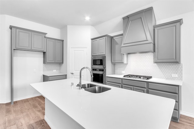 kitchen featuring backsplash, stainless steel appliances, hardwood / wood-style flooring, premium range hood, and a center island with sink