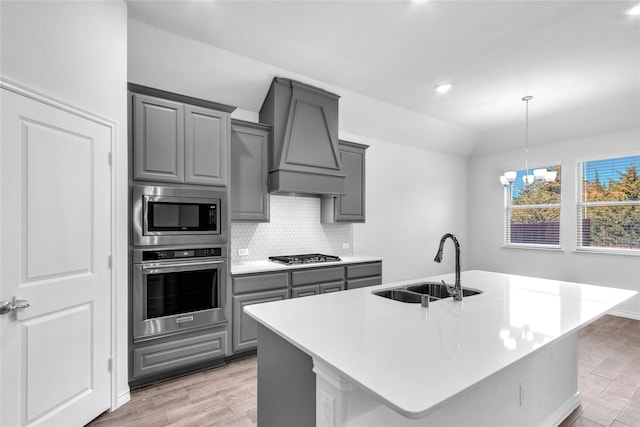 kitchen with light hardwood / wood-style flooring, stainless steel appliances, sink, and an island with sink