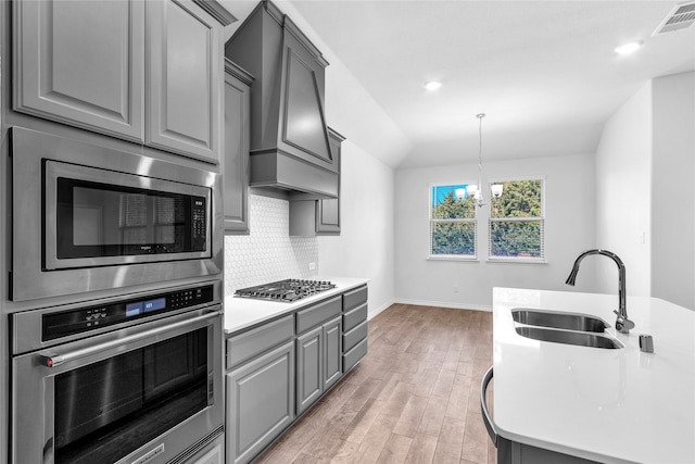 kitchen with appliances with stainless steel finishes, vaulted ceiling, light hardwood / wood-style flooring, a notable chandelier, and sink