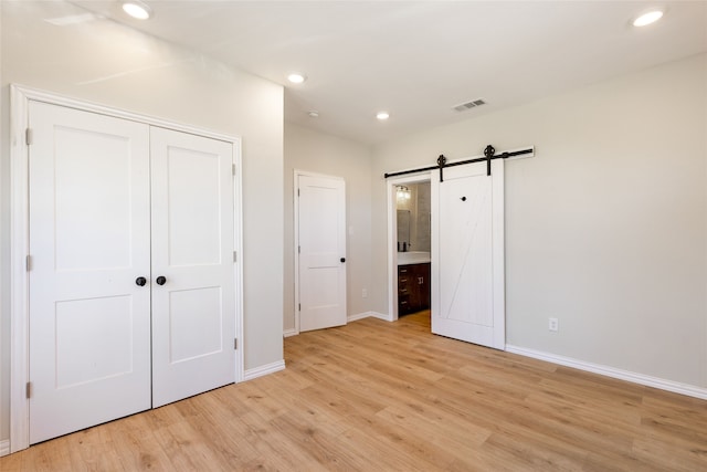 unfurnished bedroom with ensuite bath, a barn door, a closet, and light hardwood / wood-style flooring