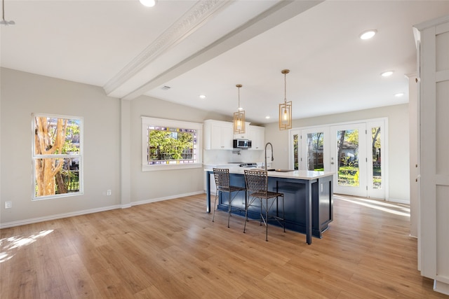 kitchen featuring a breakfast bar, a kitchen island with sink, decorative light fixtures, light hardwood / wood-style floors, and white cabinetry