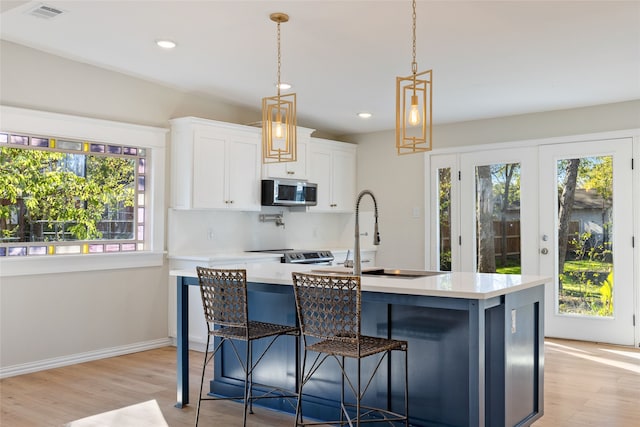 kitchen featuring stainless steel appliances, an island with sink, decorative light fixtures, a breakfast bar area, and white cabinets