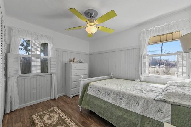 bedroom with dark wood-type flooring, ceiling fan, wood walls, and multiple windows