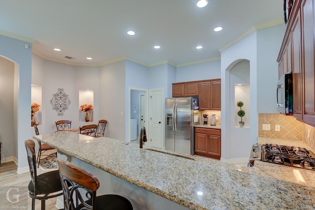 kitchen with light stone countertops, appliances with stainless steel finishes, kitchen peninsula, a kitchen breakfast bar, and decorative backsplash