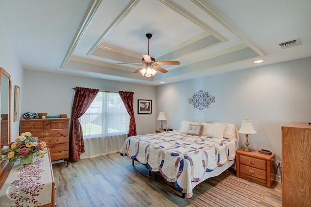 bedroom with crown molding, a tray ceiling, wood-type flooring, and ceiling fan