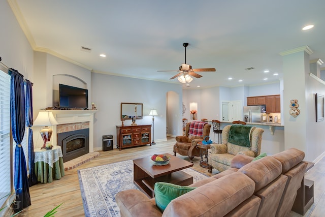 living room with crown molding, a brick fireplace, light wood-type flooring, and ceiling fan