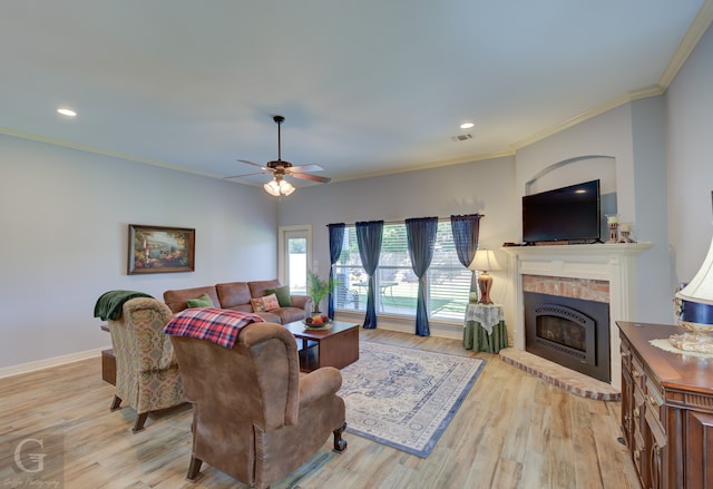 living room with light hardwood / wood-style floors, crown molding, a fireplace, and ceiling fan