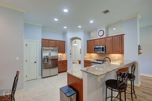 kitchen featuring stainless steel appliances, ornamental molding, a breakfast bar area, and kitchen peninsula