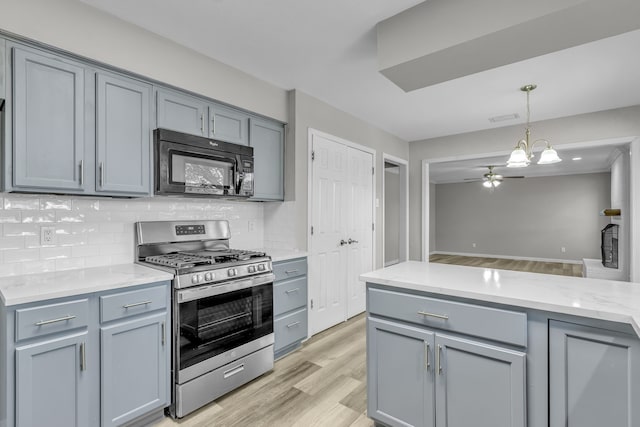 kitchen with gray cabinetry, stainless steel gas range, light wood-type flooring, and decorative light fixtures