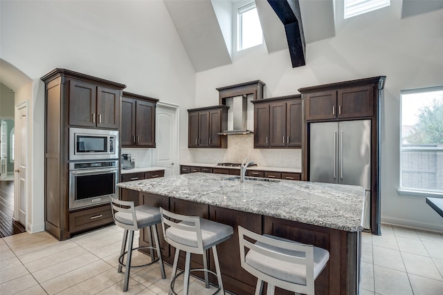 kitchen with light stone countertops, stainless steel appliances, high vaulted ceiling, a kitchen island with sink, and light tile patterned floors