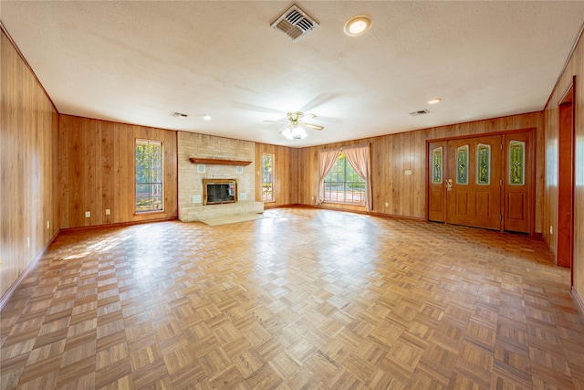 unfurnished living room featuring wood walls, a textured ceiling, parquet floors, ceiling fan, and a fireplace