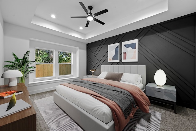 carpeted bedroom with ceiling fan and a raised ceiling