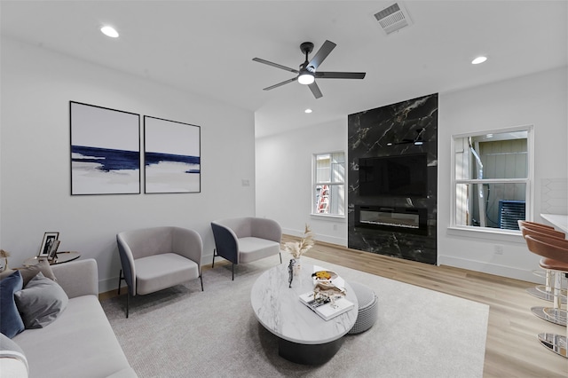 living room with light wood-type flooring, ceiling fan, and a premium fireplace