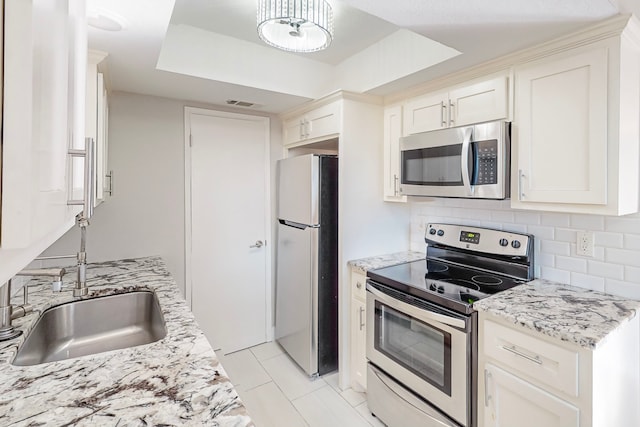 kitchen with light stone countertops, stainless steel appliances, decorative backsplash, and a tray ceiling