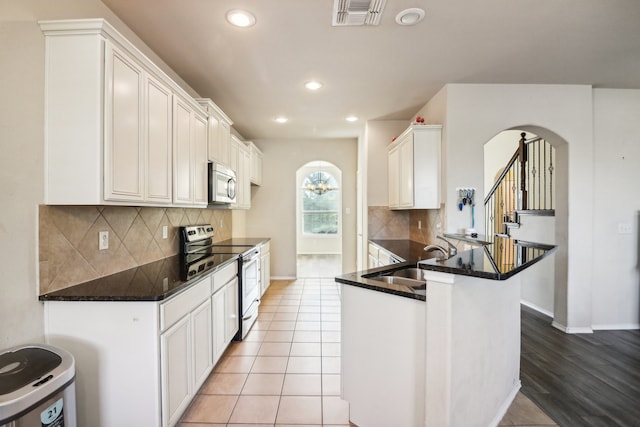 kitchen with light tile patterned flooring, sink, kitchen peninsula, stainless steel appliances, and white cabinets