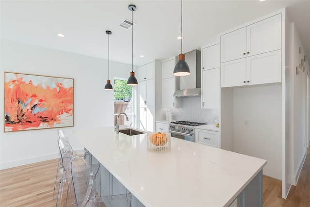 kitchen with an island with sink, high end stainless steel range, wall chimney exhaust hood, pendant lighting, and white cabinets