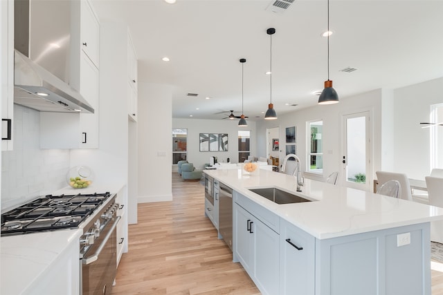 kitchen with hanging light fixtures, appliances with stainless steel finishes, white cabinetry, a kitchen island with sink, and sink