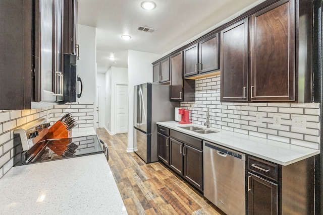 kitchen featuring decorative backsplash, hardwood / wood-style floors, light stone counters, sink, and stainless steel appliances