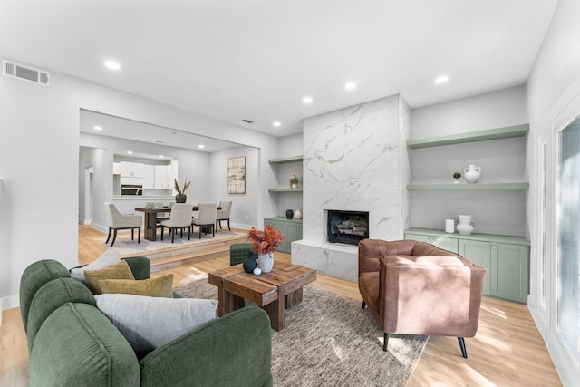 living room featuring light hardwood / wood-style flooring, a high end fireplace, and built in shelves