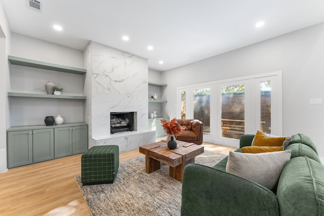 living room featuring a high end fireplace, built in features, light hardwood / wood-style floors, and french doors